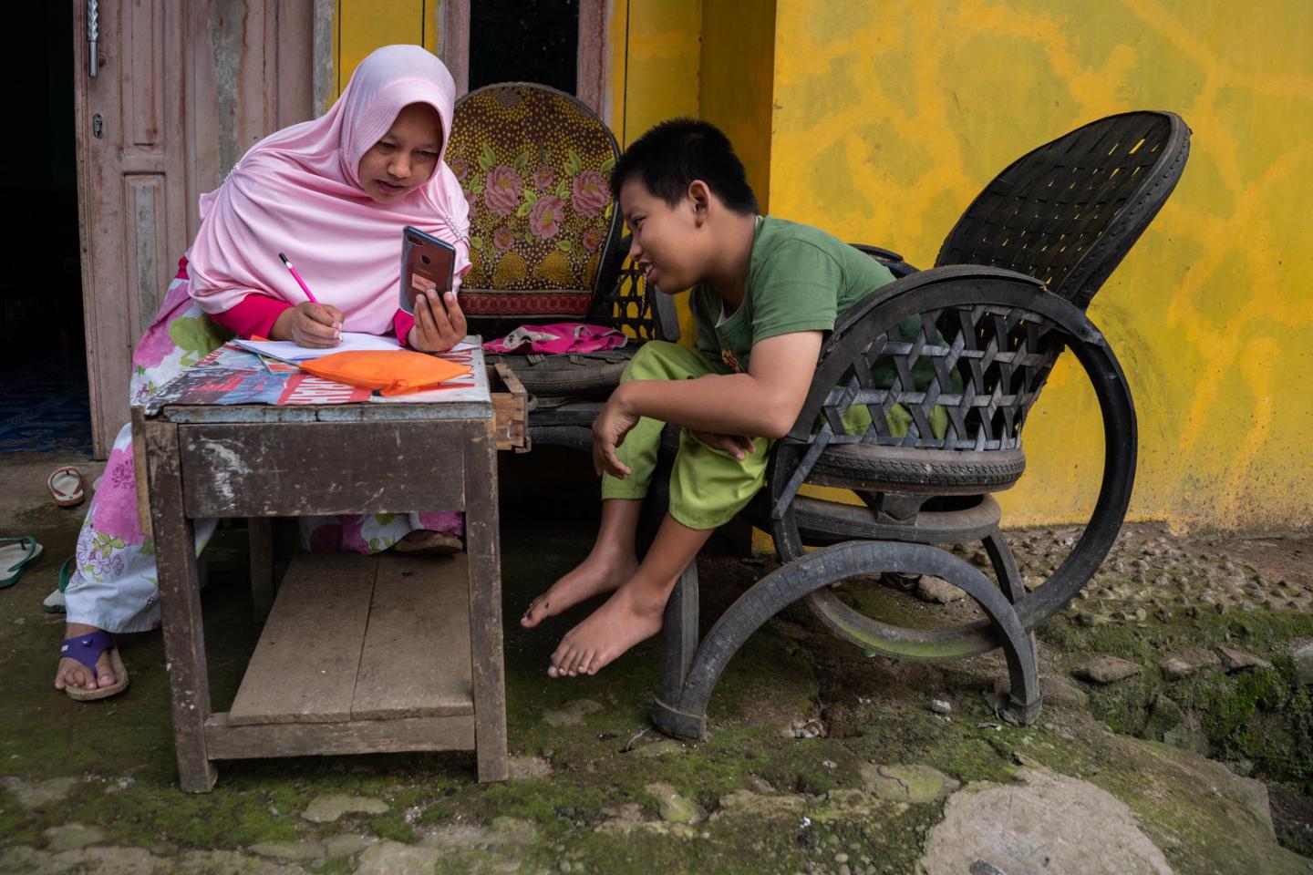 A child with a physical impairment, studies at home with his mother in Banyumas, Indonesia